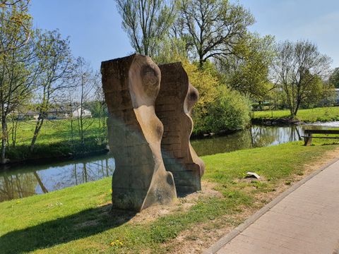 Sculpture en pierre au bord d'une rivière avec des arbres en arrière-plan.