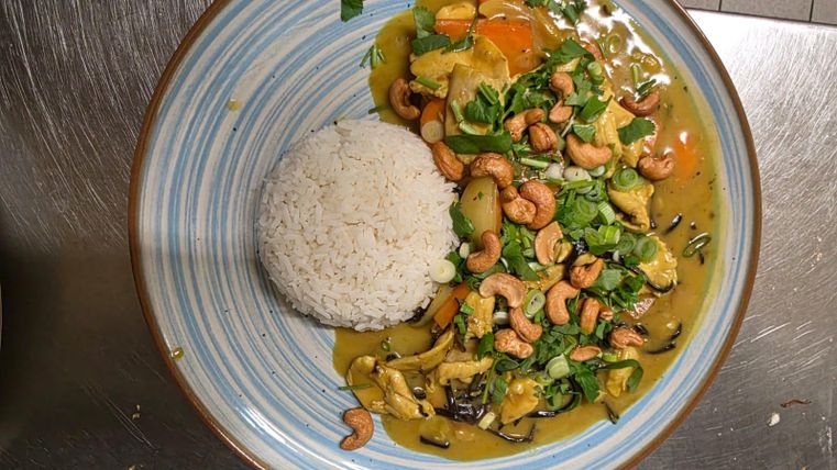 Een kleurrijk gerecht met groenten en cashewnoten, geserveerd met witte rijst. De kleuren en ingrediënten geven het eten een aantrekkelijke uitstraling.