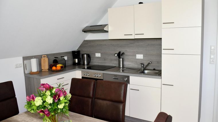 A modern kitchen with bright cabinets and a dining table. On the table sits a blooming plant and fresh fruit.