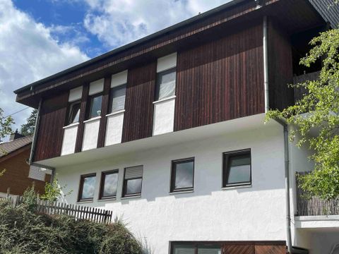 Een modern huis met een combinatie van hout- en pleistergevel. In het onderste gedeelte bevindt zich de vakantiewoning. De lucht is gedeeltelijk bewolkt en de omgeving is groen.