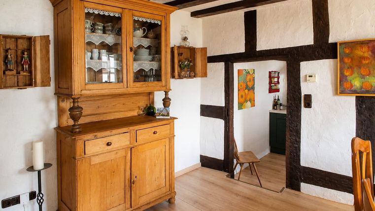 A cozy room with a wooden cabinet and a bright wooden floor. Colorful pictures hang on the walls and there is access to another corner of the room.