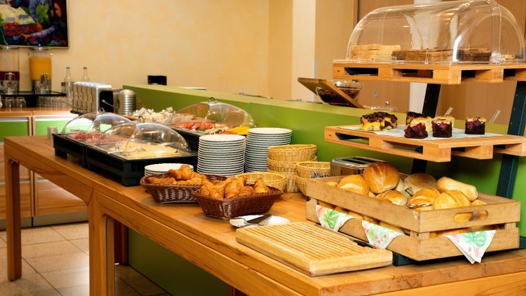 A hearty breakfast buffet with various breads, pastries, and cold cuts. The dishes are arranged on a wooden tray and in glass containers.