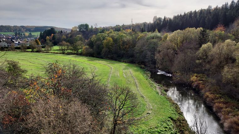 River Kyll flows through green meadows and forests, with a village in the background.