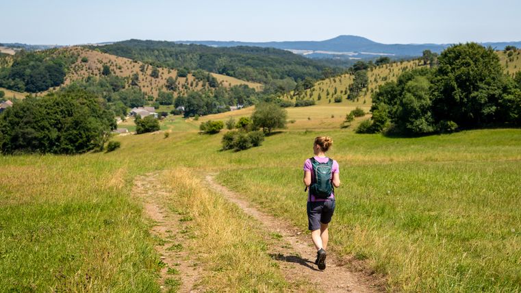 Eine Frau wandert auf einem Pfad durch eine grüne Hügellandschaft in der Eifel.