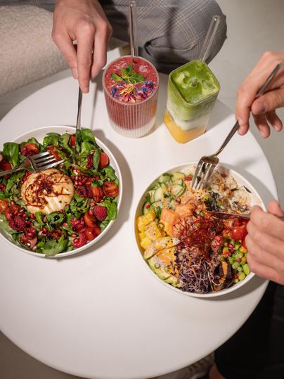 Two colorful salad bowls on a white table. Various colorful drinks in glasses are visible.