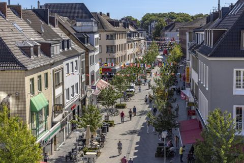 Une rue commerçante animée avec des arbres et des magasins. Beaucoup de gens flânent le long de la rue.