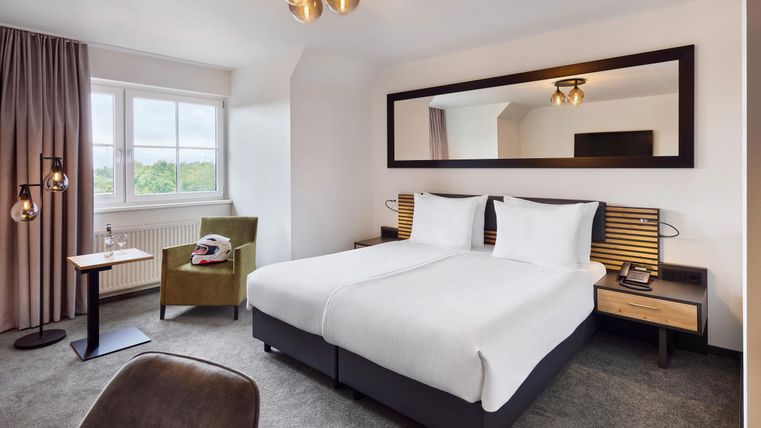 Une chambre d'hôtel moderne avec deux lits simples et un grand miroir. La chambre est lumineuse et décorée avec style, avec un fauteuil confortable et de jolis éléments de décoration.