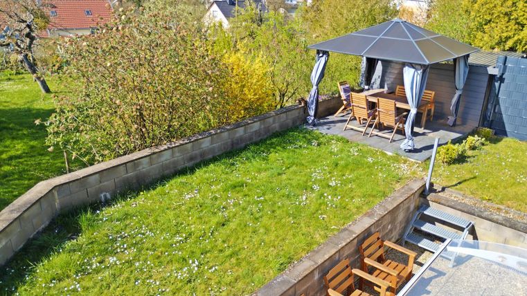 Un jardin bien entretenu avec un pavillon confortable et des meubles de jardin. En arrière-plan, des arbres et un paysage verdoyant sont visibles.