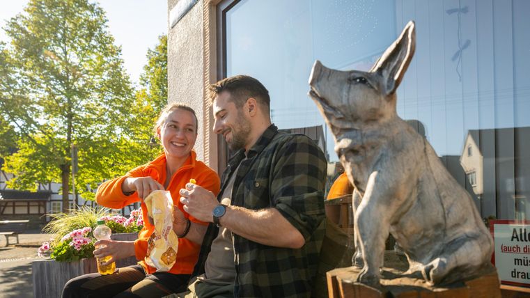 A cheerful couple sits outside next to a statue of a rabbit. They are enjoying snacks and drinks in a cozy atmosphere.