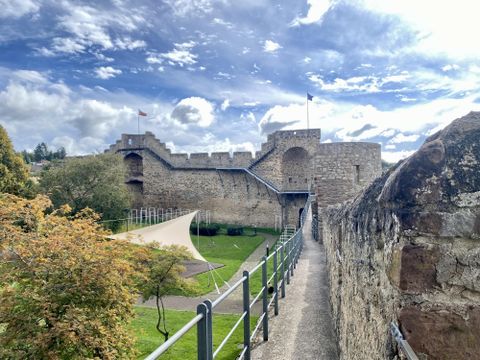 Begehbare hohe Stadtmauer aus Stein in Hillesheim mit angrenzender Parkfläche.