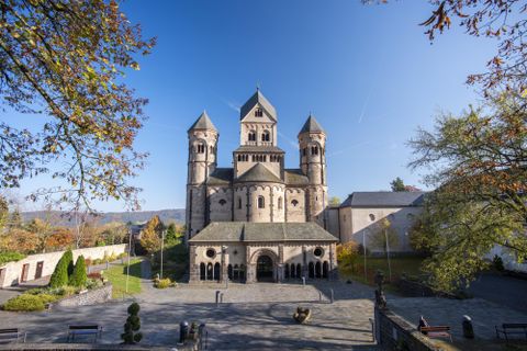 An impressive church with distinctive towers and a beautiful facade. Surrounded by green trees and a clear sky.