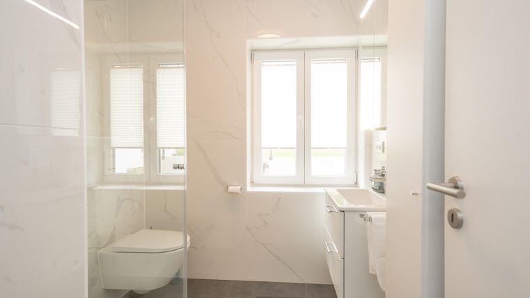 Ein modernes Badezimmer mit einer Glasdusche und hellen Wänden. Große Fenster sorgen für viel Tageslicht.