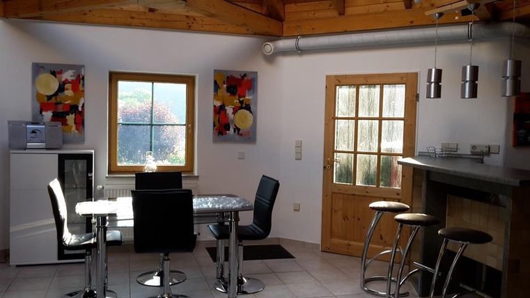 Een heldere en moderne keuken met een eettafel en stoelen. De wanden zijn versierd met kleurrijke schilderijen en een houten plafond geeft de ruimte gezelligheid.