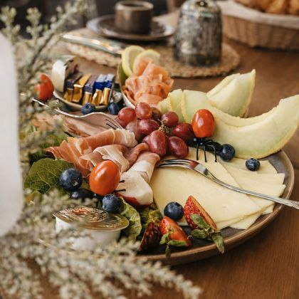Eine ansprechende Platte mit verschiedenen Käsesorten, Schinken, Trauben und Melonen. Das Arrangement ist dekorativ und einladend.