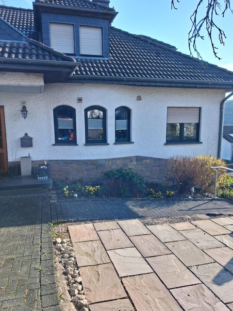 Een modern woonhuis met een geplaveide weg en een kleine tuin. De ramen zijn voorzien van jaloezieën en de gevel is lichtgekleurd.