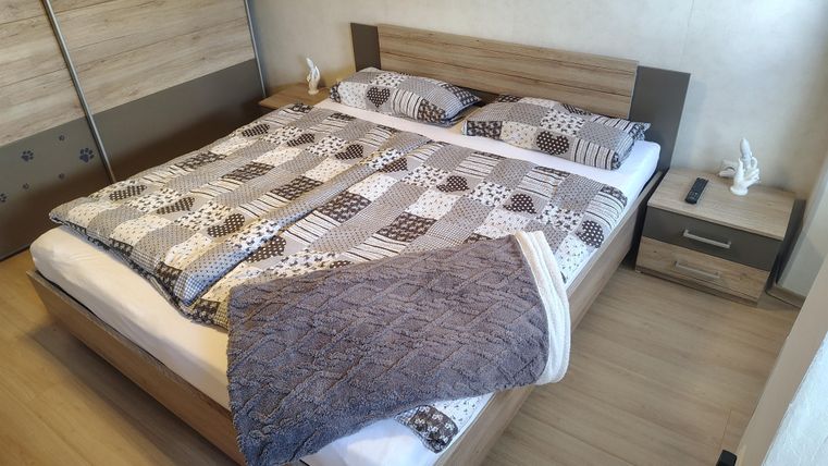 A simple bedroom with a double bed covered with patterned bedding. Next to the bed is a nightstand with a small figurine.