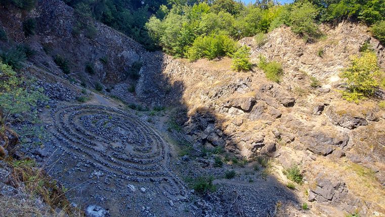 Stone labyrinth in the rocky pit of the Arensberg volcano with trees in the background.