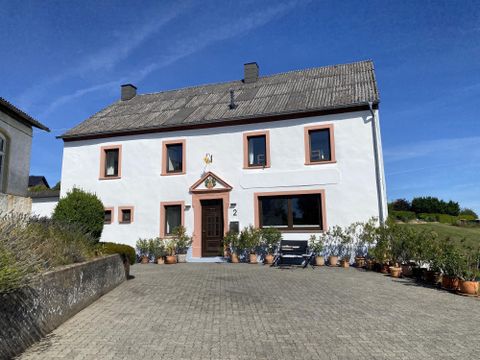 Ein hübsches Haus mit einer weißen Fassade und roten Fensterrahmen. Der Innenhof ist mit Blumentöpfen geschmückt und der Himmel ist klar und blau.