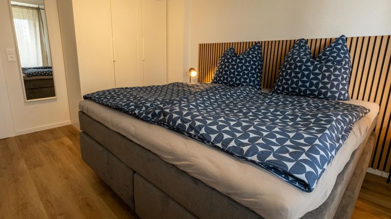Een gezellige slaapkamer met een groot bed en blauwe beddengoed. De kamer heeft lichte muren en moderne meubels.