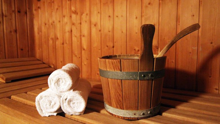 Een houten saunakruik met drie opgerolde handdoeken ligt op een bank in een sauna.