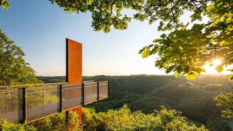 Skywalk am Eifelblick Achterhöhe mit Blick auf bewaldete Hügel bei Sonnenuntergang.