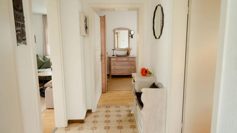 Un couloir lumineux avec un joli motif de sol.
Sur le mur, il y a des tableaux et au bout du couloir se trouve un miroir avec une table.