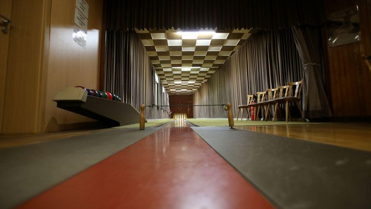 Een bowlingbaan met een rode en grijze loopbaan. Op de achtergrond zijn stoelen en gordijnen te zien.