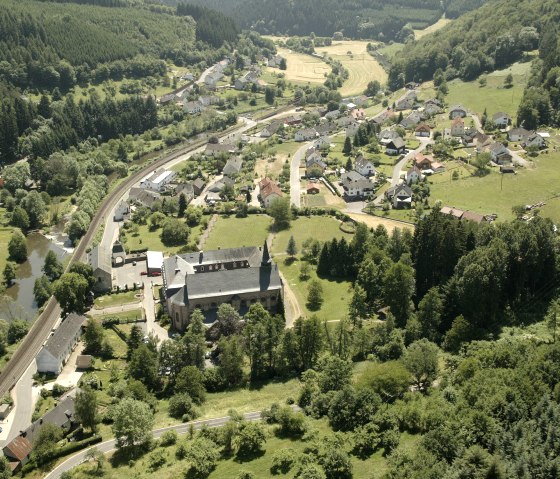 Luchtfoto van een dorp met een kerk op de voorgrond, omringd door bossen en velden. Door het dorp loopt een spoorlijn., © Rudolf Höser