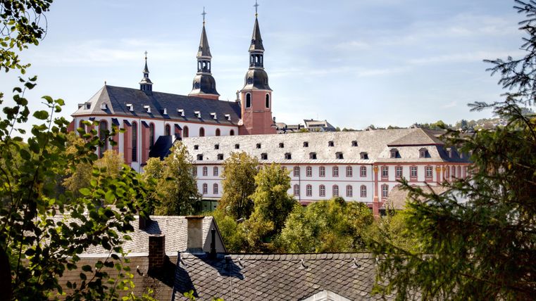 Een historisch klooster met twee markante torens. Omringd door bomen en een rustige omgeving.