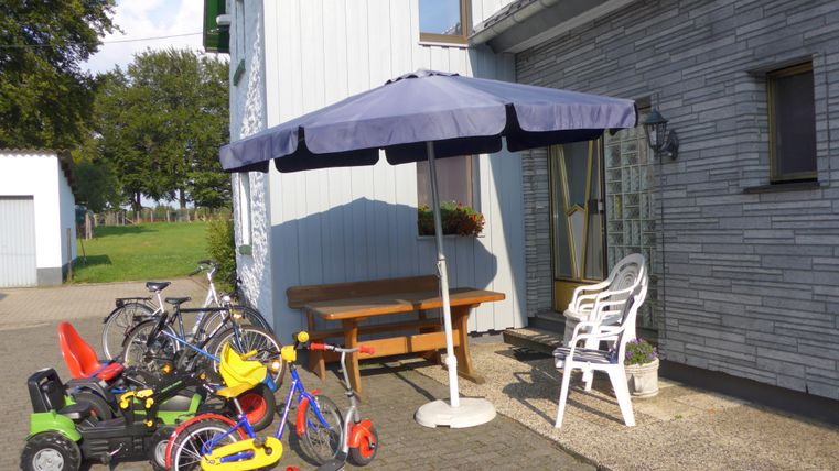 Une entrée avec un parasol et une table. À côté de l'entrée se trouvent différents jouets et vélos.