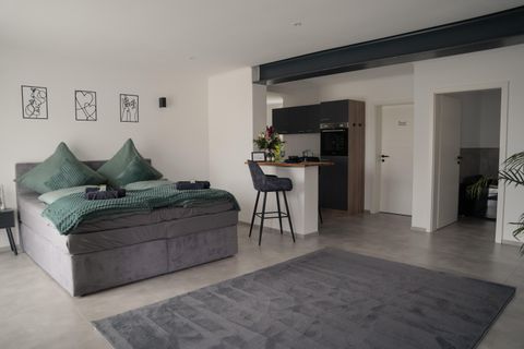 Een moderne slaapkamer met een groot, comfortabel bed en elegante decoratie. Aan een kleine bar staan stoelen en er is een verzorgde, open keuken.