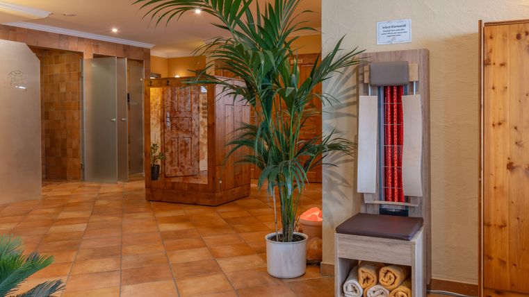 Een uitnodigende wellnessruimte met warme kleuren en veel planten. Op de achtergrond zijn douches en een infraroodstoel te zien, die een ontspannende sfeer creëren.