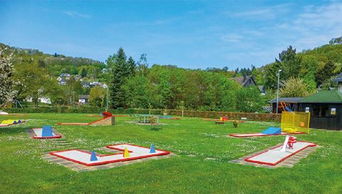 Un parcours de mini-golf dans un parc verdoyant, entouré d'arbres et de collines. Les joueurs peuvent jouer sur différents parcours.