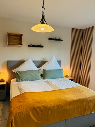 Een moderne slaapkamer met een comfortabel bed en gele accenten. De muren zijn in neutrale kleuren gehouden en er zijn warme lichtbronnen aanwezig.