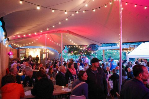 Ein geselliges Treffen mit Freunden, bei dem Sektgläser angestoßen werden. Im Hintergrund sind weitere Gäste in einem Restaurant zu sehen.