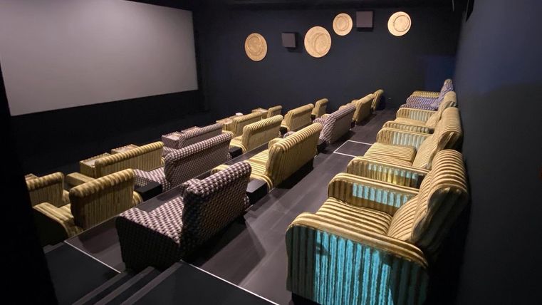 Ein gemütliches Kino mit bequemen Sitzen und einer großen Leinwand. Die Wände sind dunkel gestrichen und dekoriert.