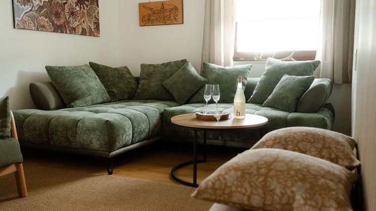 Une salon confortable avec un canapé vert et une table ronde. Sur la table se trouvent deux verres et une bouteille.