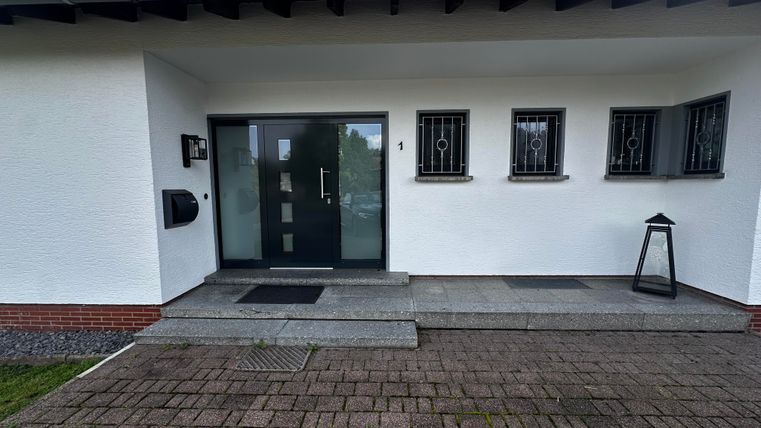 Een modern huis met een witte facade en een elegante voordeur. De entree is uitgerust met grijze tegels en een kleine lantaarn.