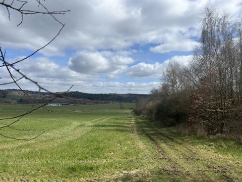 Eine Hand hält eine Glasflasche unter einem alten Wasserbrunnen. Wasser fließt aus dem Brunnen in die Flasche.