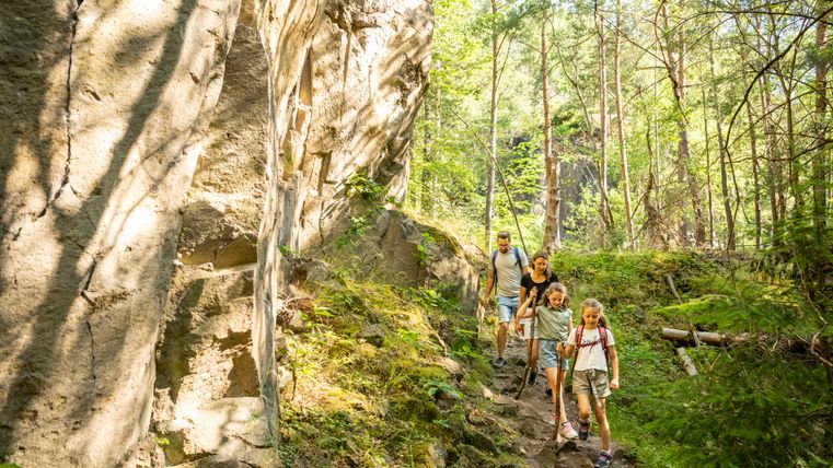 Familie wandert auf einem Waldpfad neben einer Felswand.