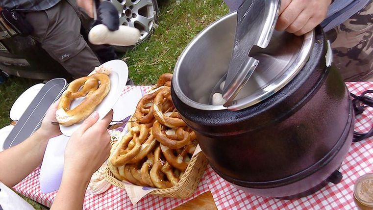Ein Stand mit frisch gebackenem Gebäck, darunter Brezeln. Menschen servieren und genießen die Snacks im Freien.