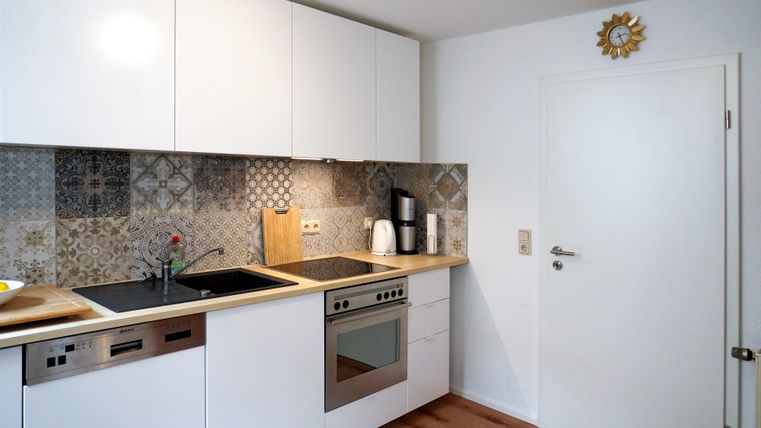 A modern kitchen with white cabinets and a decorative tiled wall. The amenities include a stove, sink, dishwasher, oven, refrigerator-freezer combination, as well as various small appliances.