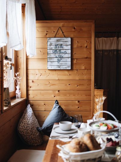 Une pièce confortable avec des murs en bois et une table sur laquelle se trouvent du pain frais et un bol de fruits. Des coussins de différentes couleurs invitent à la détente.