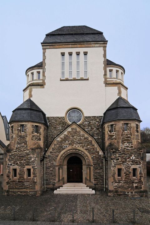 Een moderne kerk met een markante, ronde toren en stenen rondbogen. De ingang is ruim opgezet met trappen en de gevel is in lichte kleuren uitgevoerd.
