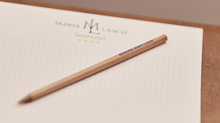 Een notitieblok met het logo van "Maria Lacz" en een houten potlood liggen op een tafel. Het blok is geruit en klaar om te schrijven.