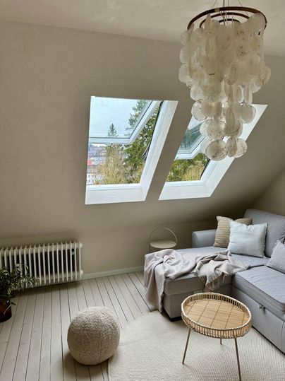 Een lichte, moderne woonkamer met dakramen en een comfortabele bank. Een ronde tafel en een zacht tapijt vullen de uitnodigende sfeer aan.