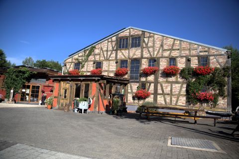 A charming half-timbered building with red flower boxes. The entrance is inviting and the surroundings are well-maintained.