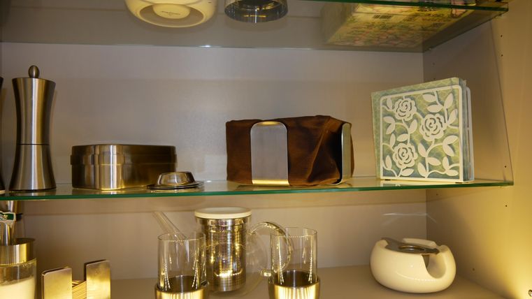 Een rek systeem met verschillende keukenhulpmiddelen en decoratieve voorwerpen. Daaronder bevinden zich glazen, een theepot en een elegant decoratieboek.