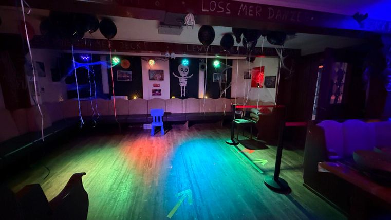 Een ruimte met kleurrijke lichten, die versierd is voor een feest. Er zijn opblaasbare objecten en een klein podium dat een feestelijke sfeer creëert.