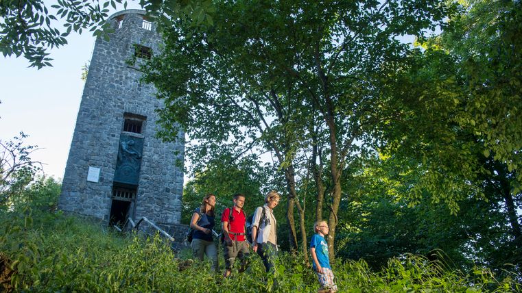 Een groep mensen daalt een beboste helling af, naast een stenen toren.